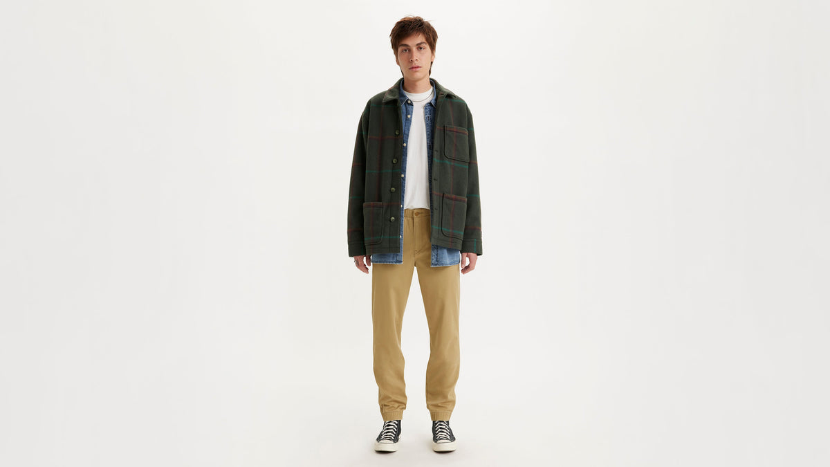 Man in tan chino jogger pants, plaid overshirt & denim layer, facing front