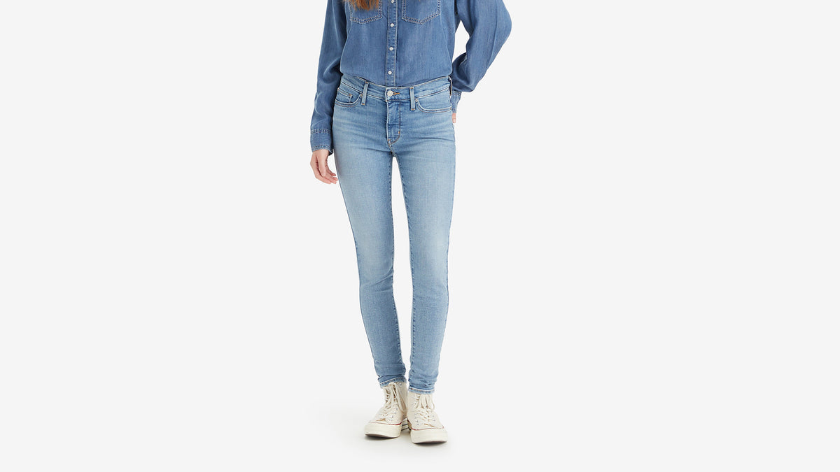 Close-up view of Levi's light-wash 310 skinny jeans with a denim shirt & white sneakers