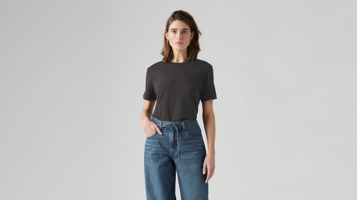 Woman stands facing forward in plain dark iconic tee & Levi’s belted straight jeans