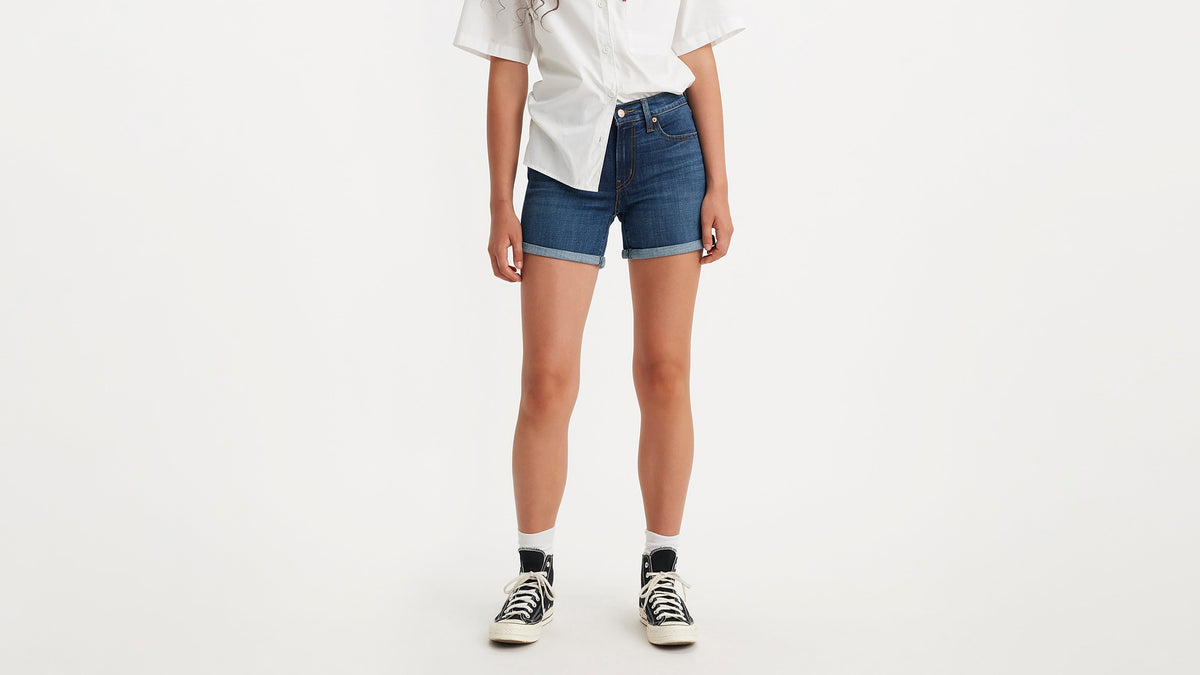 Cropped front view of a woman in a white shirt, mid-length shorts, & sneakers