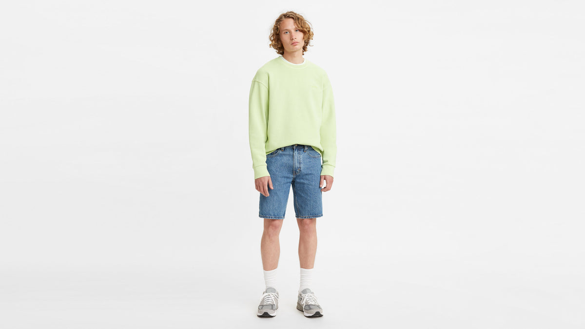 Front-facing shot of model in a pastel green sweatshirt, denim shorts, & sneakers