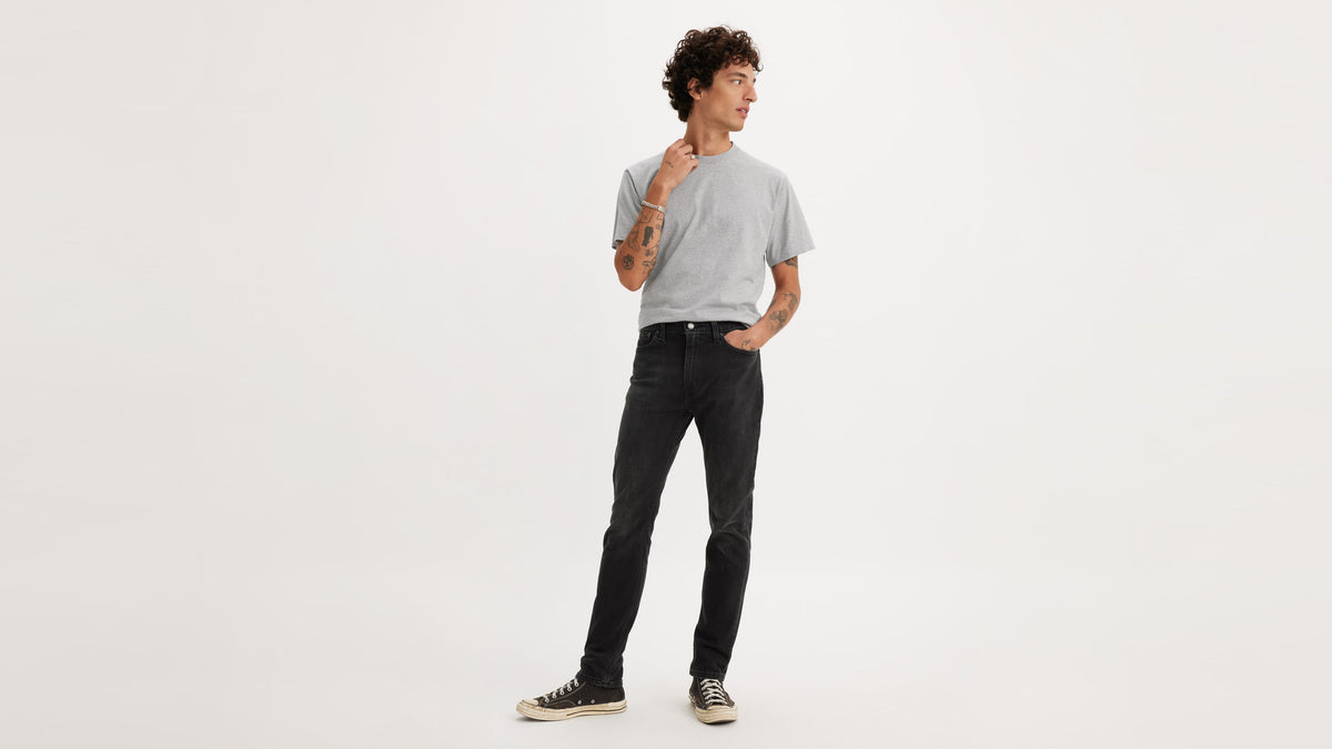 Front view of a man wearing black Levi’s 510 jeans with a grey tee & black sneakers
