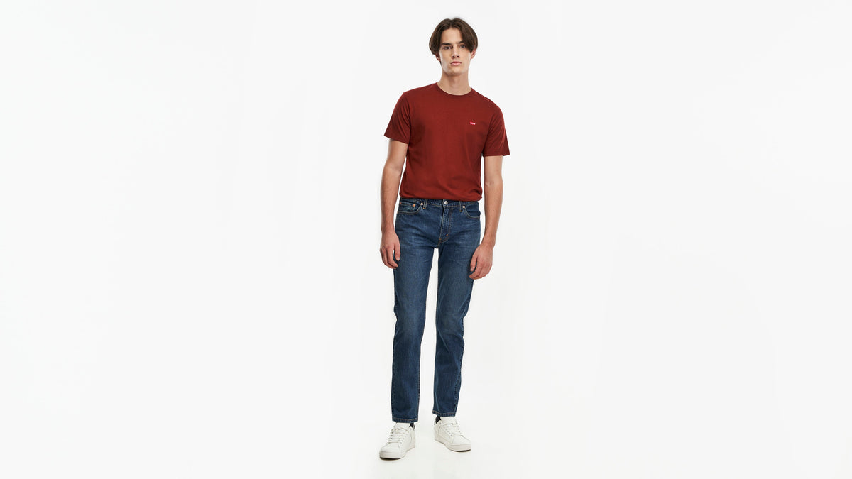 Front view of a man wearing Levi’s 511 jeans in dark blue with a red tee & sneakers