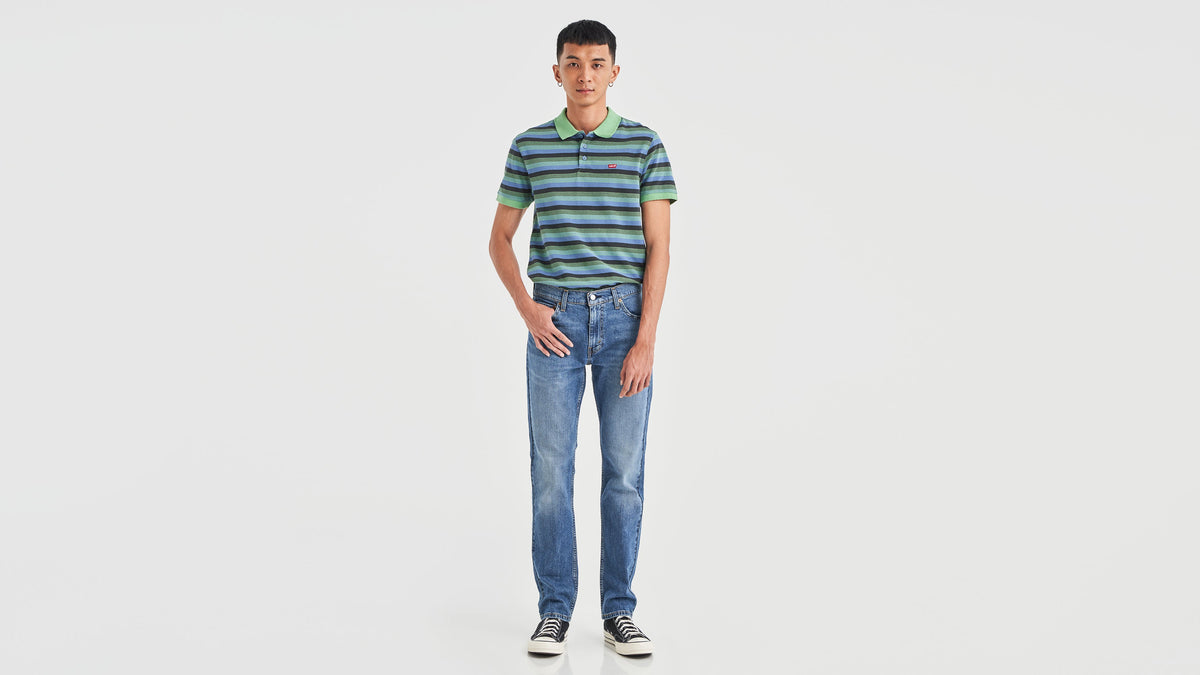 Front view of a man in striped green polo shirt, blue Levi’s 511 jeans, & sneakers