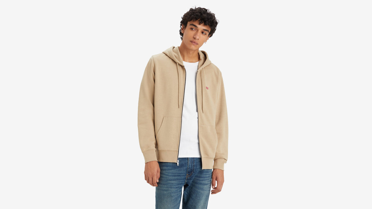 Close-up of man in beige Levi's Housemark Zip-Up Hoodie, white t-shirt, & blue jeans