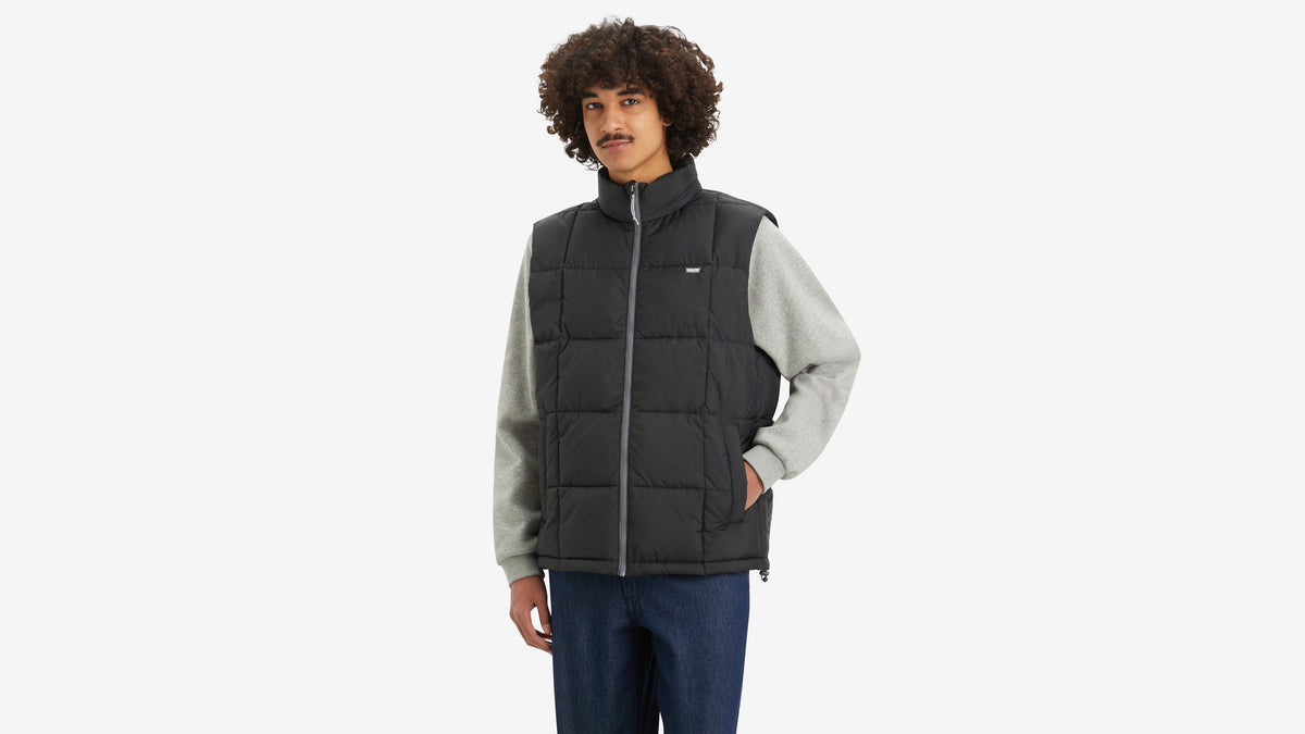 Model wearing black puffer vest over light grey sleeves and jeans