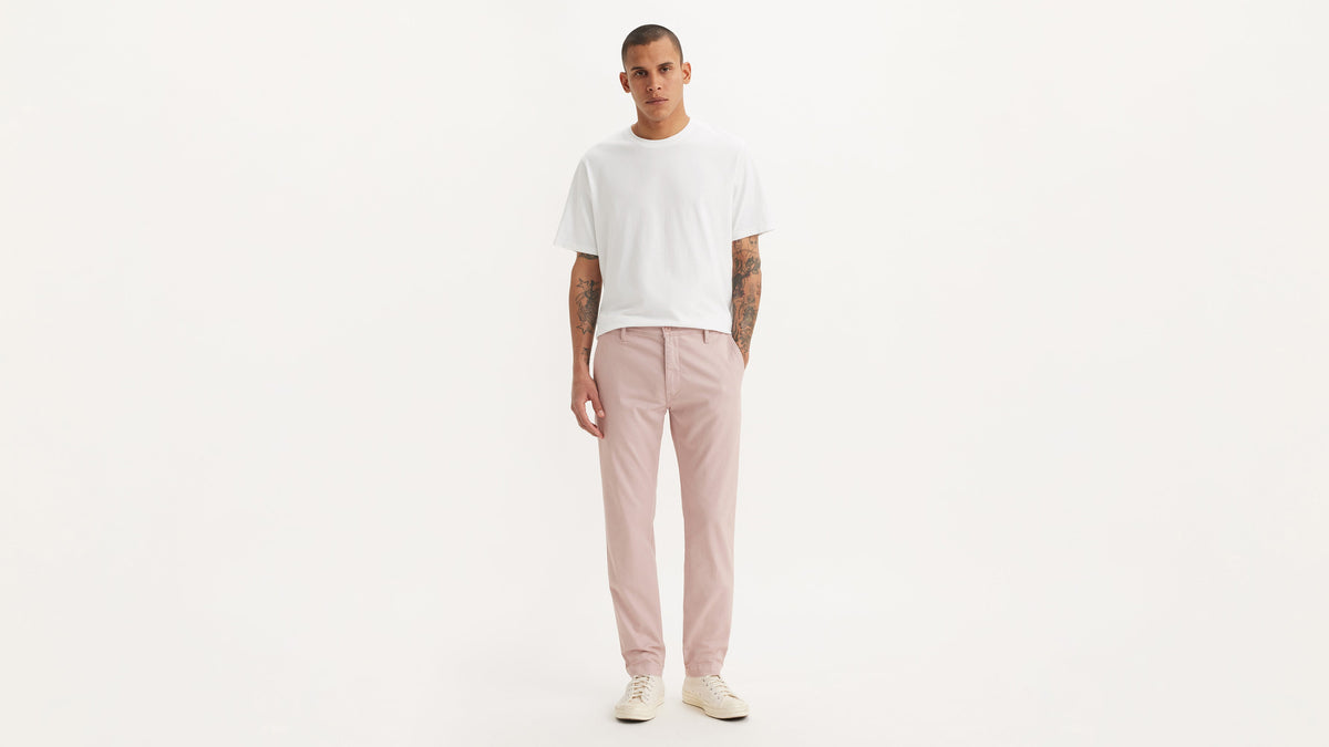 Full-body shot of man in white tee, pink Levi's chinos, & sneakers with one hand in pocket