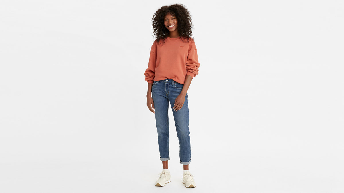 Woman in blue boyfriend jeans, rust sweatshirt, & sneakers