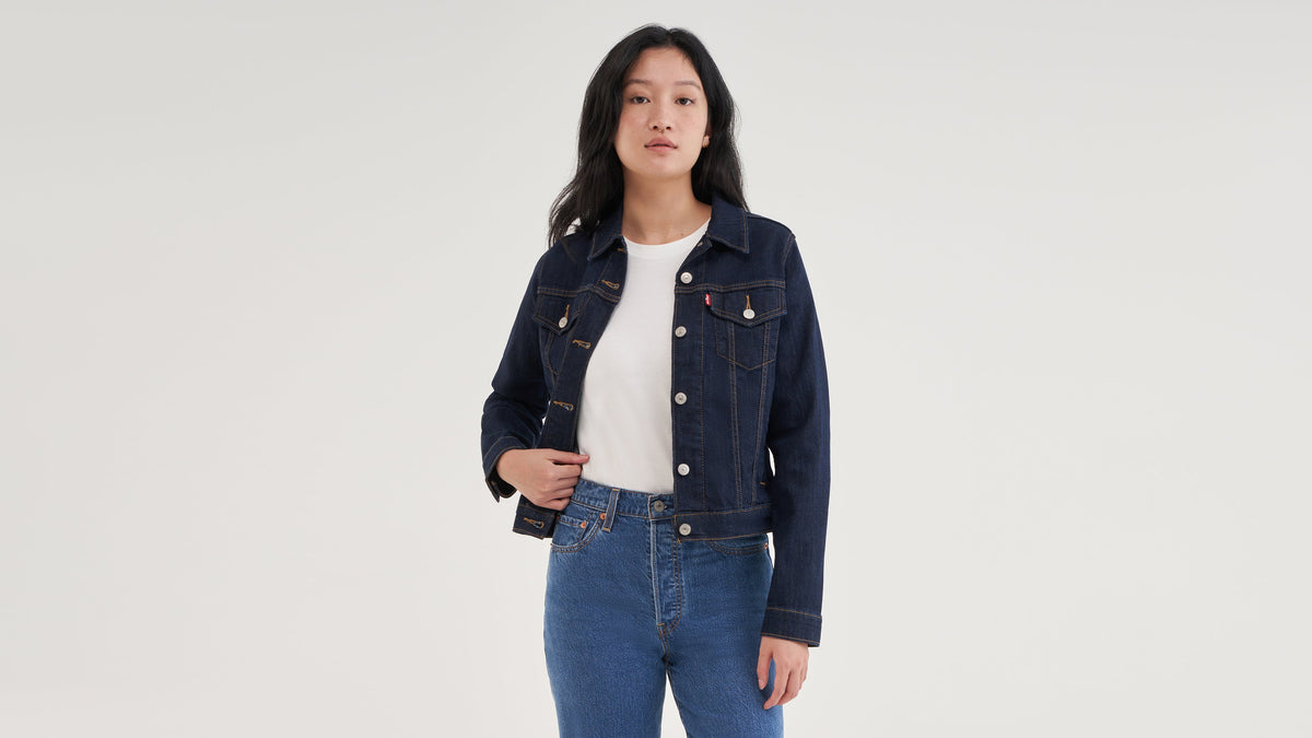 Front view of woman in layered white tee, denim trucker jacket, & jeans