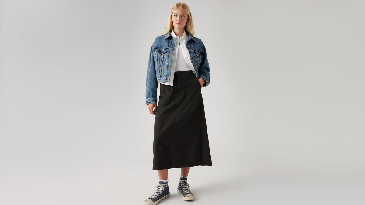 Woman in a denim jacket, white top, black surplus skirt, & sneakers